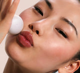 Close-up of a woman holding a white oval cosmetic container against her cheek, with the brand name YCM partially visible on the container.