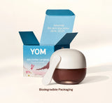 YOM 828 Loving Lip Mask jar in front of its open blue packaging box, with a white applicator spoon resting against the jar. The text 'Biodegradable Packaging' appears below.