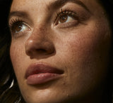 Close-up of a freckled model looking upward with glossy, hydrated lips from YOM Beauty lip mask.