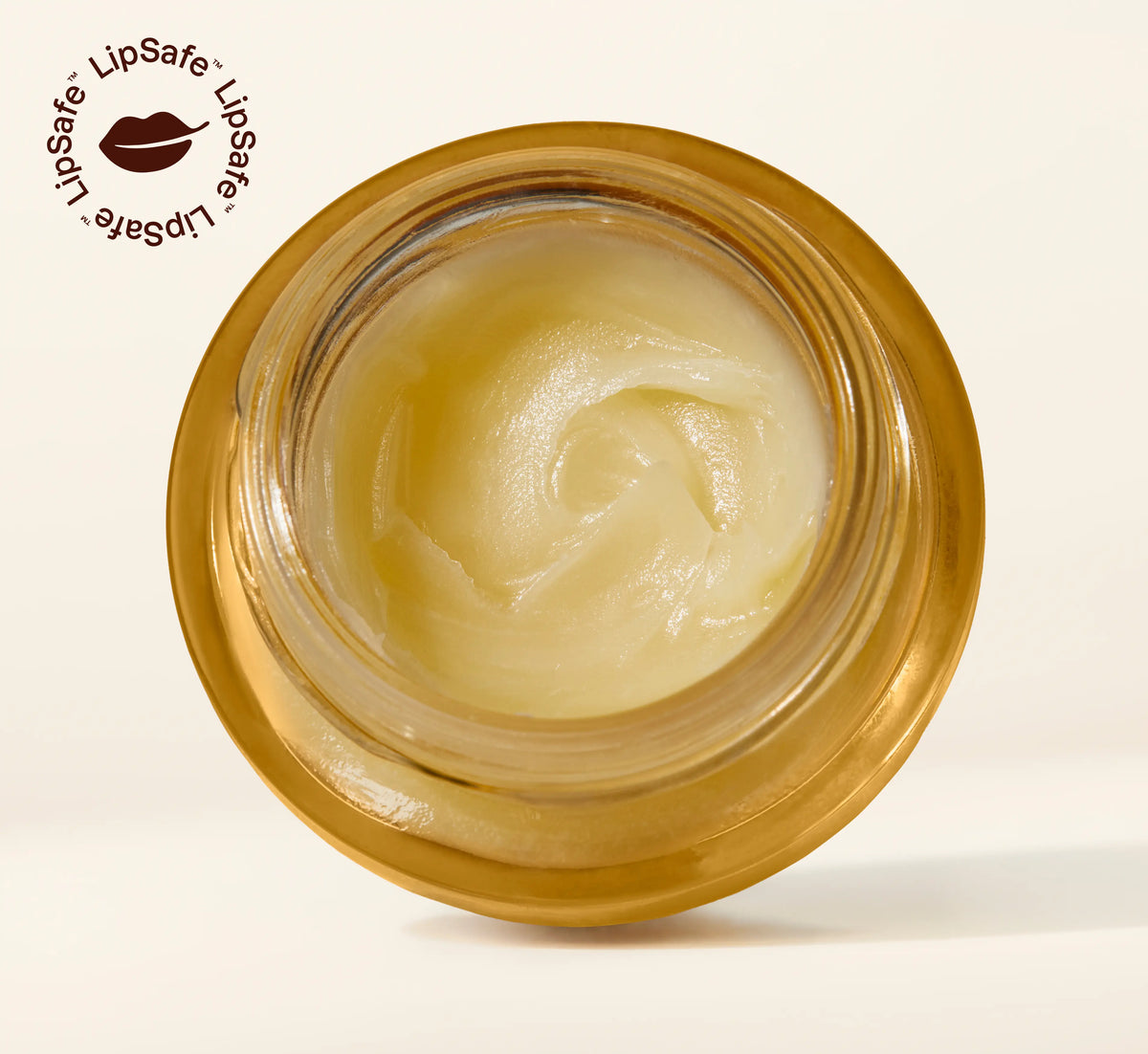 Overhead view of an open golden glass jar revealing the soft swirled texture of YOM Beauty lip balm formula with LipSafe certification logo in top corner.